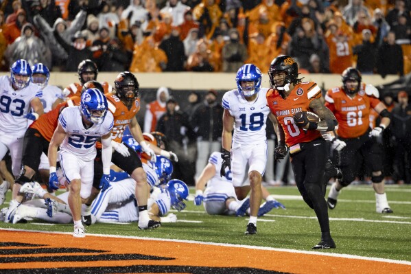 Oklahoma State running back Ollie Gordon II (0) runs past BYU linebacker Ace Kaufusi (18) and safety Talan Alfrey (25) for a touchdown in overtime of an NCAA college football game Saturday, Nov. 25, 2023, in Stillwater, Okla. (AP Photo/Mitch Alcala)