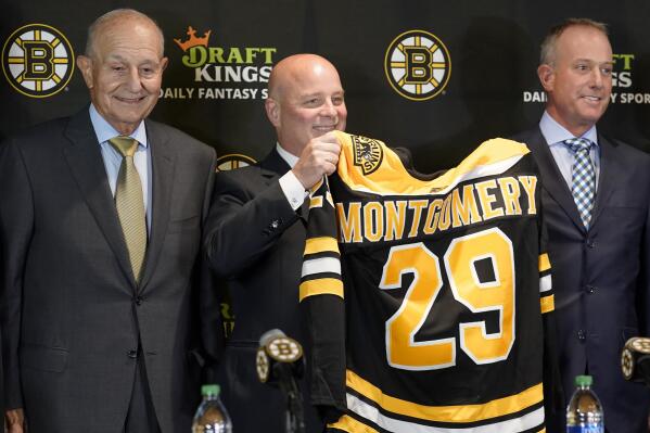Boston Bruins newly hired head coach Jim Montgomery, center, displays a Bruins jersey while standing with team owner Jeremy Jacobs, left, and CEO Charlie Jacobs, right, during a news conference, Monday, July 11, 2022, in Boston. The Bruins hired Montgomery as their new coach, giving the hockey lifer another chance at an NHL head-coaching job less than three years since he lost his first one. (AP Photo/Steven Senne)