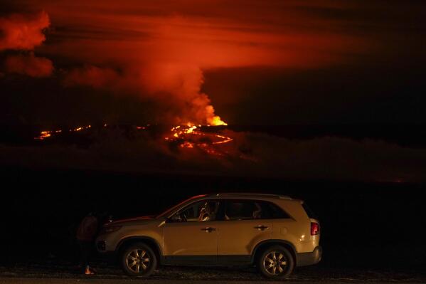 A man talks on a phone in his car alongside Saddle Road as the Mauna Loa volcano erupts Wednesday, Nov. 30, 2022, near Hilo, Hawaii. Hundreds of people in their cars lined Saddle Road, which connects the east and west sides of the island, as lava flowed down the side of Mauna Loa and could be seen fountaining into the air on Wednesday. (AP Photo/Gregory Bull)