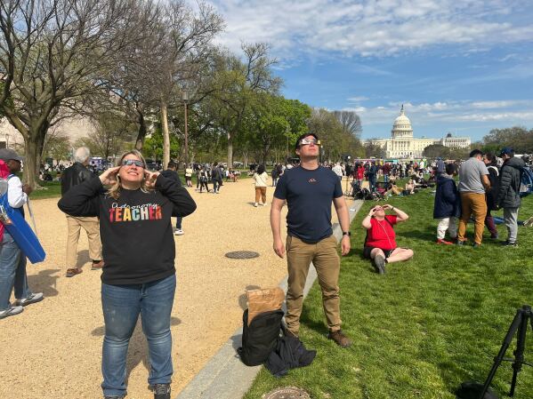 Denise Wright, wearing an “Astronomy teacher” shirt, and Crispin Burke watch the partial eclipse on the National Mall. (AP Photo/Christina Larson)