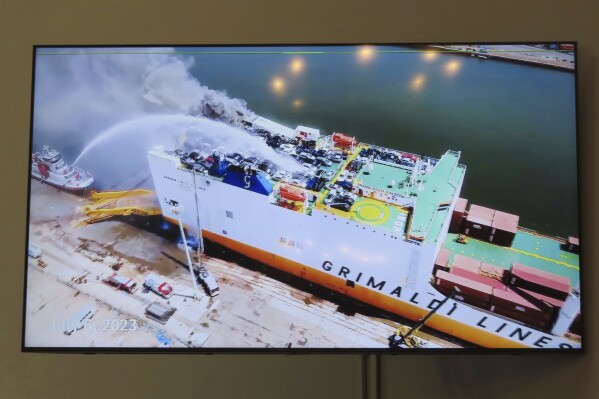 A photo displayed on a video monitor in Union,N.J., Wednesday, Jan. 10, 2024 shows a burning cargo ship in Newark N.J. on July 5, 2023. Federal investigators are conducting hearings into the blaze that killed two Newark, N.J. fire captains. (AP Photo/Wayne Parry)