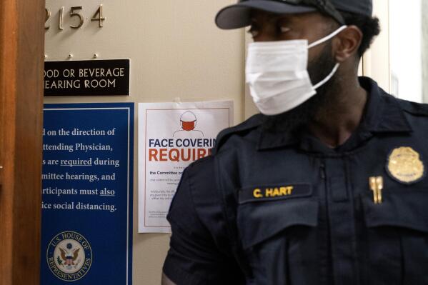 A member of the Capitol Police wears a face mask by a sign stating that face coverings are required, outside a House Committee on Oversight and Reform hearing, Thursday, July 29, 2021, on Capitol Hill in Washington. (AP Photo/Jacquelyn Martin)