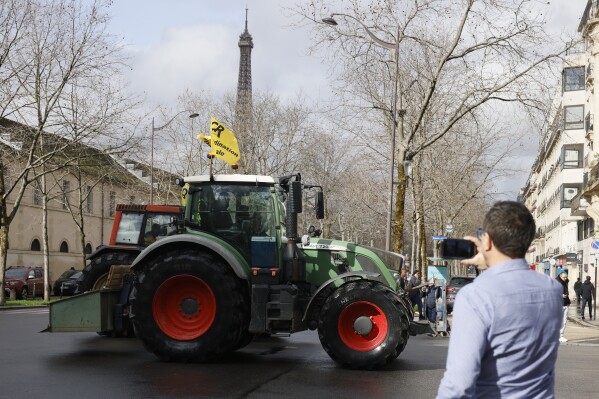 A man takes a photograph of a tractor, with the Eiffel Tower in background, Friday, Feb. 23, 2024 in Paris. Angry farmers were back to Paris on their tractors in a new protest demanding more government support and simpler regulations, on the eve of a major agricultural fair in the French capital. (AP Photo/Thomas Padilla)