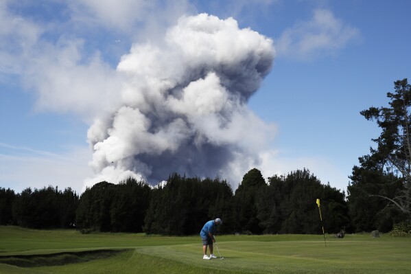 FILE - In this May 21, 2018 file photo, Doug Ralston plays golf in Volcano, Hawaii, as a huge ash plume rises from the summit of Kiluaea volcano. (AP Photo/Jae C. Hong, File)