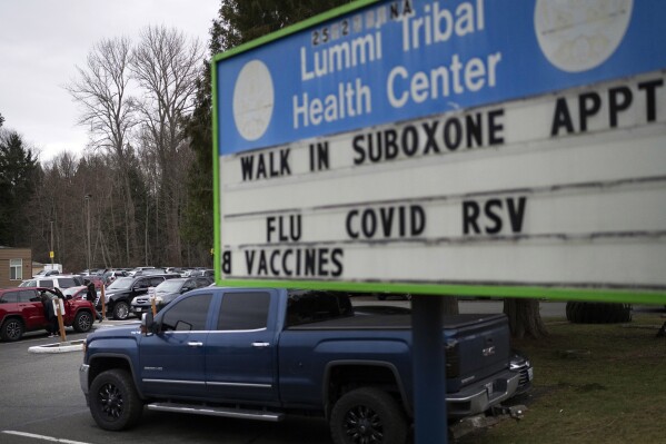 FILE - People walk through the parking lot of the Lummi Tribal Health Center advertising walk-in appointments for Suboxone, a medicine used to treat opioid dependence, on the Lummi Reservation, Feb. 8, 2024, near Bellingham, Wash. On Tuesday, March 20, 2024, Washington Gov. Jay Inslee has signed a multimillion-dollar measure to send state money to tribes and Indigenous people in the state who die from opioid overdoses at disproportionately high rates in Washington. (AP Photo/Lindsey Wasson, File)