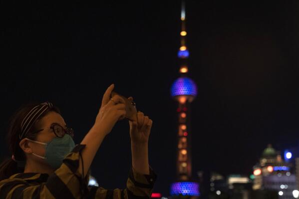 A woman takes photos near the Oriental Pearl Tower on the bund, Tuesday, May 31, 2022, in Shanghai. Shanghai authorities say they will take major steps Wednesday toward reopening China's largest city after a two-month COVID-19 lockdown that has set back the national economy and largely confined millions of people to their homes. (AP Photo/Ng Han Guan)