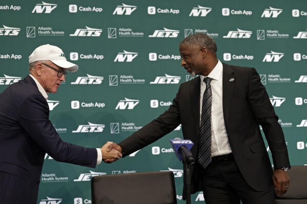 New York Jets new head coach Aaron Glenn, right, shakes hands with team owner Woody Johnson, left, during a news conference at the NFL football team's training facility Jan. 27, 2025, in Florham Park, N.J. (AP Photo/Adam Hunger,File)