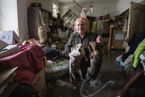 Local resident Tetiana holds her pets, Tsatsa and Chunya, as she stands inside her house that was flooded after the Kakhovka dam blew up overnight, in Kherson, Ukraine, Tuesday, June 6, 2023. (AP Photo/Evgeniy Maloletka)