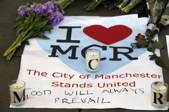 FILE - In this Tuesday May 23, 2017 file photo, a sign with flowers and candles are placed after a vigil in Albert Square, Manchester, England, the day after the suicide attack at an Ariana Grande concert that left 22 people dead. A public inquiry into a mass attack at a 2017 Ariana Grade concert in northwest England concluded Thursday June 17, 2021, that “serious shortcomings” by venue operators, security staff and police helped a suicide bomber who killed 22 people carry out his “evil intentions." (AP Photo/Kirsty Wigglesworth, File)