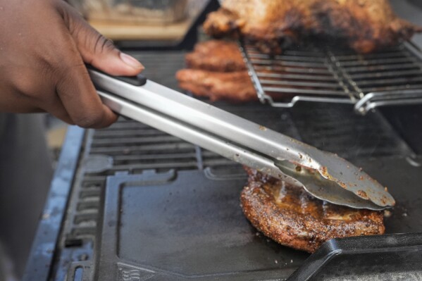 Eric Farley, of the Boys and Girls Club, sears a piece of grilled pork at the World Championship Barbecue Cooking Contest, Friday, May 17, 2024, in Memphis, Tenn. (AP Photo/George Walker IV)