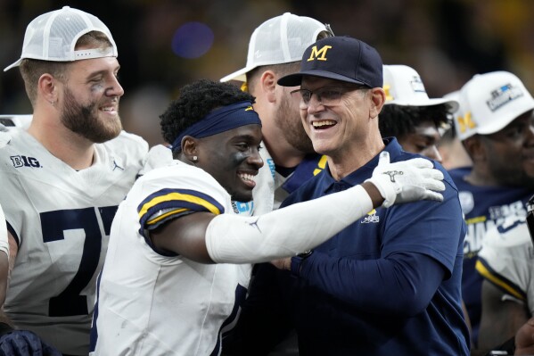 Michigan defensive back Mike Sainristil (0) celebrates with head coach Jim Harbaugh after the Big Ten championship NCAA college football game against Iowa, Saturday, Dec. 2, 2023, in Indianapolis. Michigan won 26-0. (AP Photo/AJ Mast)