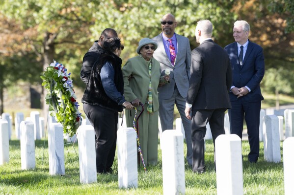 Joann Woodson keeps a flower after placing a wreath at the headstone of her husband Cpl. Waverly B. Woodson Jr. during a ceremony at Arlington National Cemetery on Tuesday, Oct. 11, 2023 in Arlington, Va. During the D-Day invasion, the landing craft Cpl. Waverly B. Woodson Jr. was in took heavy fire and he was wounded before even getting to the beach, but for the next 30 hours he treated 200 wounded men while under intense small arms and artillery fire before collapsing from his injuries and blood loss, according to accounts of his service. With Joann Woodson, are her son, Steve Woodson, center, and Sen. Chris Van Hollen, D-Md. (AP Photo/Kevin Wolf)
