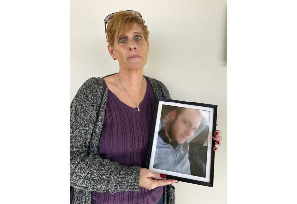 Heather DeWolf holds up a photo of her late son, Zach DeWolf, who died in 2020 at age 33, Tuesday, Dec. 5, 2023, in Colorado Springs, Colo. Colorado's Return to Nature Funeral Home, where 190 decaying bodies were found in October, handled his remains. Now, DeWolf fears the ashes she received from the funeral home are not her son's and that his body was instead part of the grim discovery. (AP Photo/Jesse Bedayn)