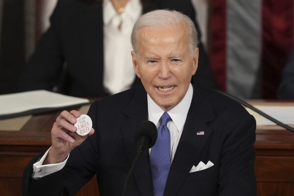 President Joe Biden holds up a Laken Riley button as he delivers the State of the Union address to a joint session of Congress at the U.S. Capitol, Thursday March 7, 2024, in Washington. (AP Photo/Andrew Harnik)
