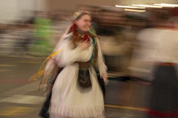 A woman wearing a traditional Ukrainian costume dances with others at a market in Kyiv, Ukraine, Sunday, April 28, 2024. (AP Photo/Francisco Seco)