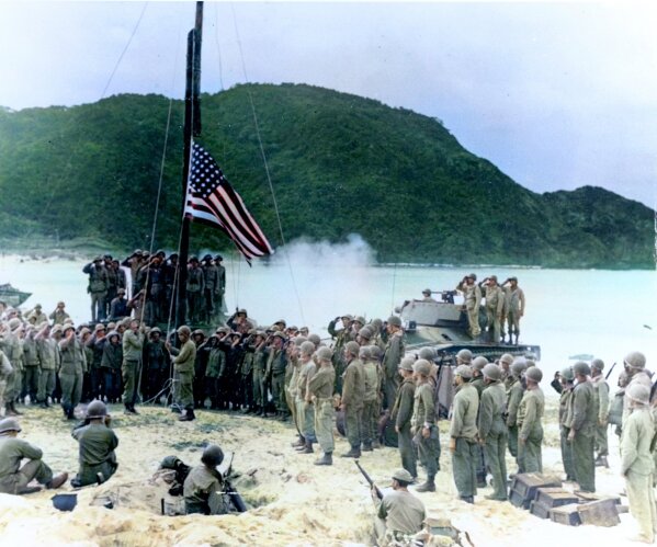 In this black and white photo digitally colorized and published in 2020 by Anju Niwata and Hidenori Watanave,  U.S. Army and Coast Guardsmen stand at attention as the American flag is raised over Akashima, Japan on April 2, 1945, the little island, only a few miles from Okinawa. Niwata and Watanave are adding color to pre-war and wartime photographs using a combination of methods. These include AI technologies, but also traditional methods to fill the gaps in automated coloring. These include going door to door interviewing survivors who track back childhood memories, and communicating on social media to gather information from a wider audience. The team has brought to life more than a thousand black-and-white photographs that illustrate the pre-war lives of ordinary people and chronicles the onset and destruction caused by World War II. (U.S. Coast Guard/Navy Radiophoto/Anju Niwata & Hidenori Watanave via AP)