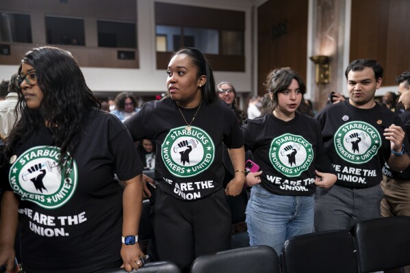 File - Advocates for a union for Starbucks employees watch as company founder Howard Schultz leaves a hearing after testifying to the Senate Health, Education, Labor and Pensions Committee at the Capitol in Washington on March 29, 2023. Starbucks says it’s committed to bargaining with unionized workers and reaching labor agreements next year. The move Friday is major reversal for the coffee chain after two years fighting the unionization of its U.S. stores. (AP Photo/J. Scott Applewhite, File)