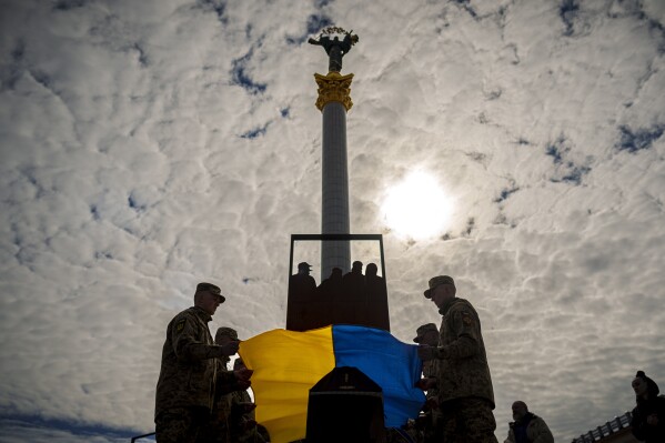 Ukrainian servicemen place the national flag on the coffin of their fallen fellow Vadym Popelniuk, born in 1991, during a religious service in Independence Square in Kyiv, Ukraine, Friday, April 5, 2024. (AP Photo/Vadim Ghirda)