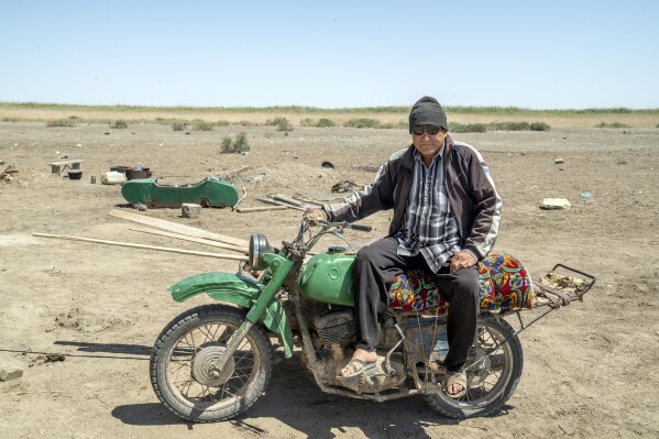 A man poses for a photo on his motorcycle next to his desert home while guarding the lands and destroyed houses that have been abandoned after the drying up of the Aral Sea, outside Muynak, Uzbekistan, Saturday, June 24, 2023. (AP Photo/Ebrahim Noroozi)