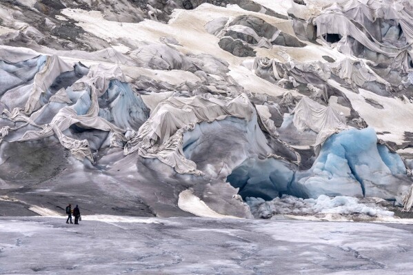 FILE - Team members of ETH (Swiss Federal Institute of Technology) glaciologist and head of the Swiss measurement network 'Glamos', Matthias Huss, arrive at the Rhone Glacier partially covered near Goms, Switzerland, June 16, 2023. The U.N. weather agency is reporting that glaciers shrank more than ever from 2011 and 2020, as it released its latest stark report about the fallout on the planet from climate change. (APPhoto/Matthias Schrader, File)