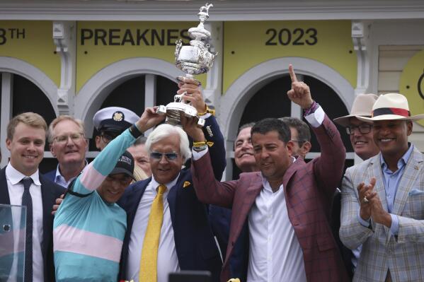 RETRANSMISSION TO CORRECT NAME OF AWARD TO WOODLAWN VASE - Bob Baffert, center, trainer of National Treasure, and jockey John Velazquez, left, help hoist the Woodlawn Vase after winning the148th running of the Preakness Stakes horse race at Pimlico Race Course, Saturday, May 20, 2023, in Baltimore. (AP Photo/Julia Nikhinson)