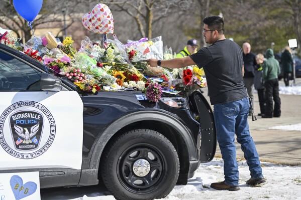 Crasto Cruz Reyes of Austin, Minn., places flowers at one of the three memorial vehicles in front of the Burnsville Police Department in Burnsville, Minn., Monday, Feb. 19, 2024. Two police officers and a firefighter who responded to a domestic situation at a suburban Minneapolis home were killed early Sunday during a standoff by a heavily armed man who shot at police from the home where seven children were also inside. (Craig Lassig/Pioneer Press via AP)