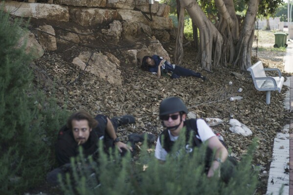 Journalists take cover as a siren warns of incoming rockets fired from the Gaza Strip at Kibbutz Netiv Haasara, Israel, Friday, Nov. 17, 2023. (AP Photo/Leo Correa)