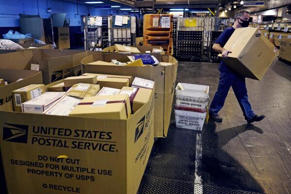 A worker carries a large parcel at the United States Postal Service sorting and processing facility, Thursday, Nov. 18, 2021, in Boston. Last year's holiday season was far from the most wonderful time of the year for the beleaguered U.S. Postal Service. Shippers are now gearing up for another holiday crush.(AP Photo/Charles Krupa)
