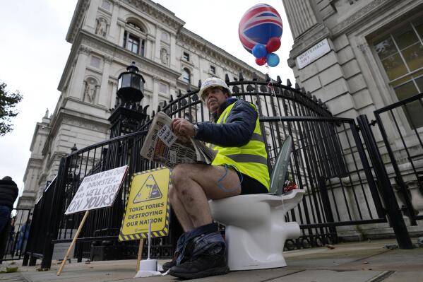 FILE - An activist sits on a toilet at the entrance to Downing Street to protest against raw sewage dumping in the rivers and seas around the UK in London, on Oct. 26, 2021. EU lawmakers have a new, post-Brexit reason to be annoyed with Britain: British sewage overflows seeping into the English Channel and North Sea. (AP Photo/Frank Augstein)