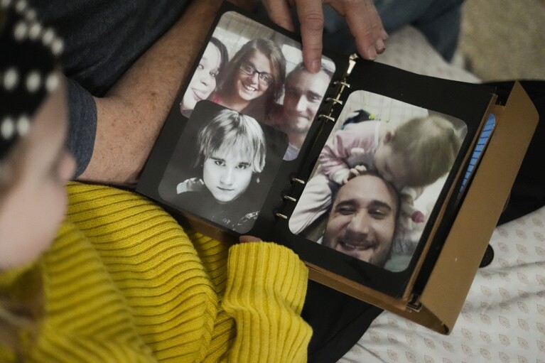 Estella Baraniak, 8, sits with her grandfather Brian Baraniak and looks at a family photo album with images of her deceased father, Matthew Baraniak, in Halifax, Pa., March 6, 2024. (AP Photo/Matt Rourke)
