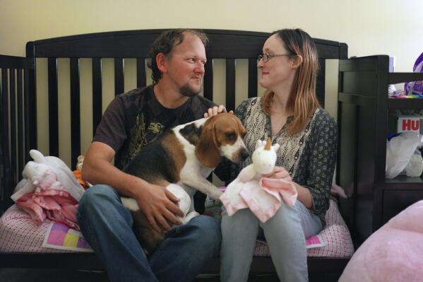 Andrew and Lauren Hackney sit in their daughter's room with their dog Scrappy after one of their twice-weekly supervised visits, in Oakdale, Pa., on Thursday, Nov. 17, 2022. At 7 months old, the couple had difficulty feeding their daughter and brought her to the children's hospital in Pittsburgh. They believe hospital staff alerted the Allegheny County Department of Human Services because the baby was severely dehydrated and malnourished, which resulted in removing the young child from their custody. The Hackneys and their lawyer believe the Allegheny County Family Screening tool may have flagged the couple as dangerous because of their disabilities. Over a year later, they continue to fight for custody of their child. (AP Photo/Jessie Wardarski)