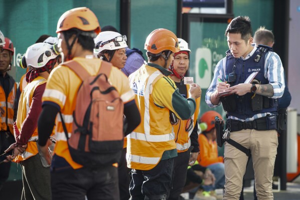 Police interview construction workers in the central business district following a shooting in Auckland, New Zealand, Thursday, July 20, 2023. A gunman killed and injured people at a construction site in New Zealand’s largest city, as the nation prepared to host games in the FIFA Women’s World Cup soccer tournament, authorities said. (Jason Oxenham/New Zealand Herald via AP)