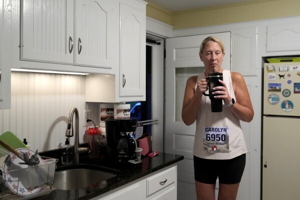 Carolyn Baker, a runner who suffered from heatstroke last year, drinks water in her kitchen before heading out to run in the Falmouth Road Race, Sunday, Aug. 18, 2024, in Falmouth, Mass. (AP Photo/Jeff Roberson)