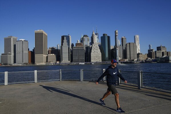 A pedestrian walks along an empty Pier 2 in Brooklyn Bridge Park against the downtown Manhattan skyline, Monday, March 16, 2020, in New York.  New York leaders took a series of unprecedented steps Sunday to slow the spread of the coronavirus, including canceling schools and extinguishing most nightlife in New York City.The vast majority of people recover from the new coronavirus. According to the World  Health Organization, most people recover in about two to six weeks, depending on the severity of the illness. (AP Photo/John Minchillo)
