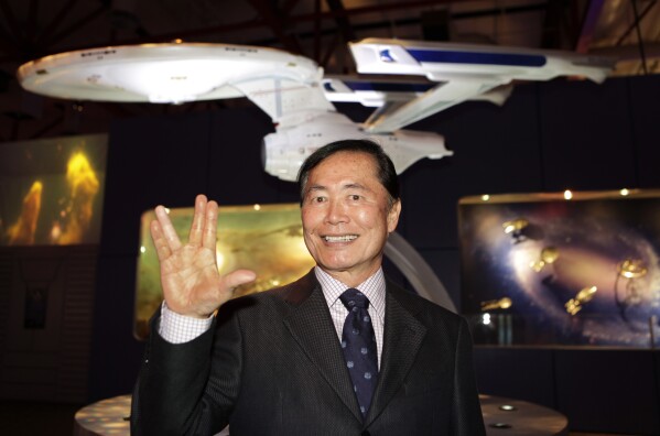 FILE - Actor George Takei, who played the role of helm officer Sulu in the original television series, "Star Trek," gives a "live long and prosper" gesture in front of a model of the U.S.S. Enterprise space ship at an exhibit at the Tech Museum in San Jose, Calif., on Oct. 20, 2009. (AP Photo/Paul Sakuma, File)