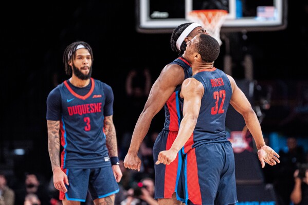 Duquesne's Kareem Rozier (32) celebrates with Jimmy Clark III, center, during the first half of an NCAA college basketball game against VCU in the championship of the Atlantic 10 Conference tournament on Sunday, March 17, 2024, in New York. (AP Photo/Peter K. Afriyie)