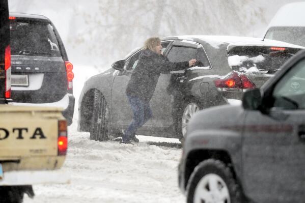 A woman tries to push a stuck car in the snow at the intersection of State Street and Divide Avenue in Bismarck, N.D., Tuesday, April 12, 2022. (Mike McCleary/The Bismarck Tribune via AP)