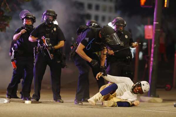 FILE - Denver Police Department officers clear a man who fell to the street after they used tear gas and rubber bullets to disperse a protest outside the Colorado Capitol in Denver, May 28, 2020, over the death of George Floyd. Denver will pay $4.7 million to settle a class action lawsuit that alleged that protesters were unjustly targeted for violating the city's curfew during demonstrations over the killing of Floyd in 2020. City councilors unanimously agreed to the deal Monday, Aug. 28, 2023, without any debate. (AP Photo/David Zalubowski, File)