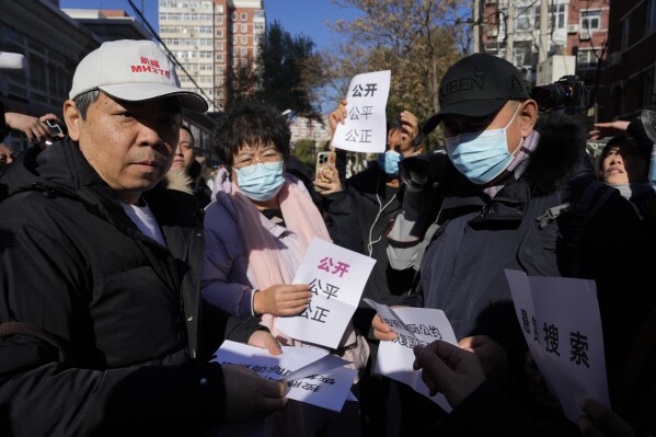 Jiang Hui, left, whose mother was on the missing MH370 airline, wears a cap which reads "Pray for Blessing MH370" as he distributes papers with the words " Open, Fair and Just" during a meeting with journalists in Beijing, Monday, Nov. 27, 2023. A Beijing court is holding compensation hearings for Chinese relatives of people who died on a Malaysia Airlines plane that disappeared in 2014 on a flight to Beijing. (AP Photo/Ng Han Guan)