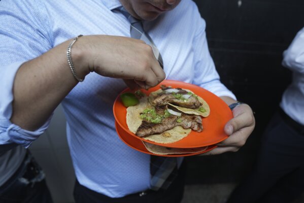 A customer finishes squeezing lime juice on his tacos at the Tacos El Califa de León stand, in Mexico City, Wednesday, May 15, 2024. Tacos El Califa de León is the first ever taco stand to receive a Michelin star from the French dining guide. (AP Photo/Fernando Llano)