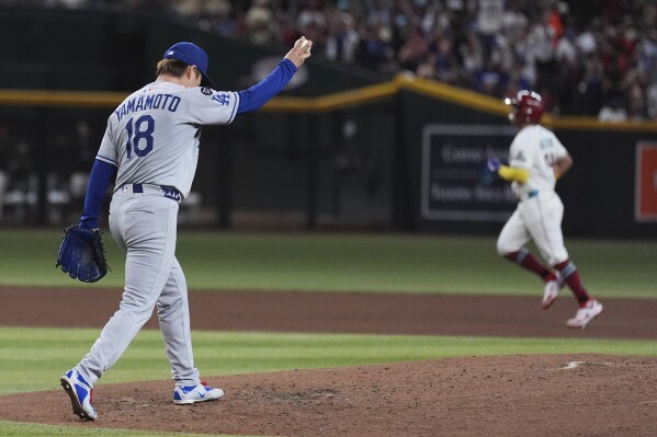 Los Angeles Dodgers starting pitcher Yoshinobu Yamamoto (18), of Japan, holds a new ball after giving up a grand slam to Arizona Diamondbacks' Gabriel Moreno, right, during the fourth inning of a baseball game Thursday, May 8, 2025, in Phoenix. (AP Photo/Ross D. Franklin)