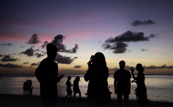 People watch the sun set along a popular beach in Tamuning, Guam, Monday, May 6, 2019. Isolated on an emerald green hunk of volcanic rock closer to Tokyo than Honolulu, Guamanians often like to joke that whatever happens on the mainland takes a long time to reach them. While the U.S. Catholic Church has been roiled by the child sexual abuse scandal for nearly two decades, the island's faithful are still reckoning with new revelations from survivors long shamed into silence by men who claimed divine authority to cloak their sins. (AP Photo/David Goldman)