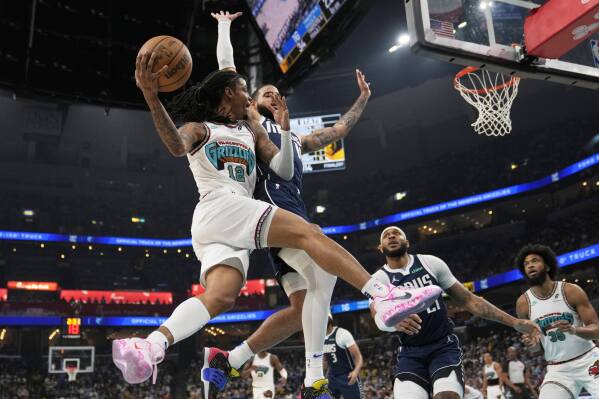 Memphis Grizzlies guard Ja Morant (12)- passes the ball around Dallas Mavericks forward Caleb Martin, right, during the first half of an NBA play-in tournament basketball game Friday, April 18, 2025, in Memphis, Tenn. (AP Photo/George Walker IV)