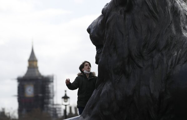 A boy climbs onto part of Nelson's Column and looks at one of the four lion statues at the base of the column with the Queen Elizabeth II tower in the background in London, Saturday, March 27, 2021. The Queen Elizabeth II tower contains the bell known as Big Ben and is currently undergoing a major refurbishment. (AP Photo/Alastair Grant)