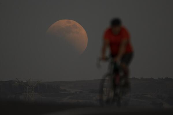 A lunar eclipse is seen behind a cyclist during the first blood moon of the year, in Irwindale, Calif., Sunday, May 15, 2022. (AP Photo/Ringo H.W. Chiu)