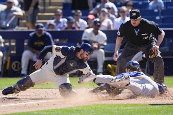 Los Angeles Dodgers' James Outman, bottom right, is tagged out stealing home by Milwaukee Brewers catcher Eric Haase, left, during the third inning of a spring training baseball game, Saturday, March 2, 2024, in Phoenix. Umpire John Bacon watches the play. (AP Photo/Carolyn Kaster)