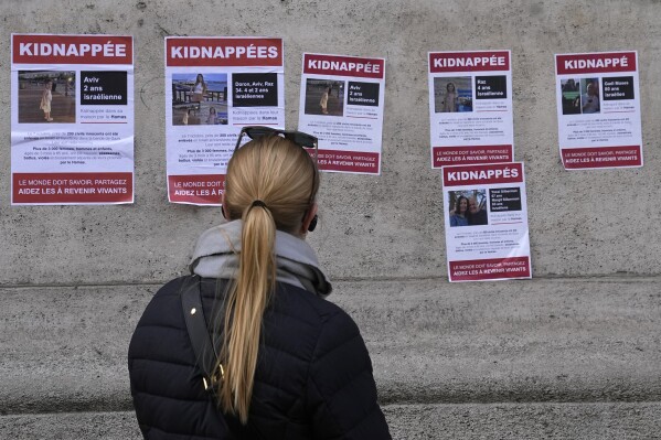 A woman watches posters pasted by the UEJF (Union of Jewish French Students) Monday, Oct. 16, 2023 in Paris. The images across Paris show of Jewish missing persons held by Hamas in Gaza. (AP Photo/Michel Euler)