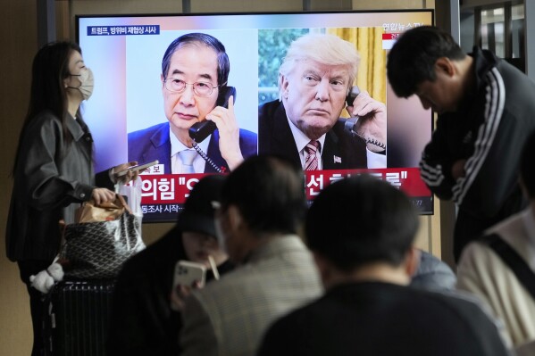 People watch a TV screen showing a file image of South Korean acting President Han Duck-soo and U.S. President Donald Trump, right, during a news program at the Seoul Railway Station in Seoul, South Korea, Wednesday, April 9, 2025. (AP Photo/Ahn Young-joon)