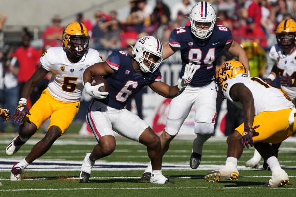 Arizona running back Michael Wiley (6) runs the ball between Arizona State defensive backs Chris Edmonds (5) and Khoury Bethley (15) in the first half of an NCAA college football game, Friday, Nov. 25, 2022, in Tucson, Ariz. (AP Photo/Rick Scuteri)