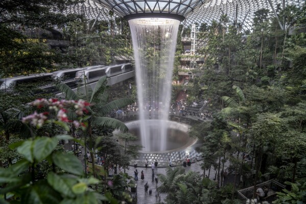 Visitors walk through the Jewel as a Skytrain shuttles passengers between terminals at Changi Airport, Sunday, July 16, 2023, in Singapore. The Jewel complex boasts the world's tallest indoor waterfall surrounded by a five story indoor garden with thousands of trees, plants, ferns and shrubs. (AP Photo/David Goldman)